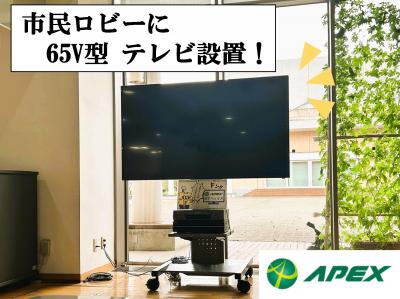 写真の真ん中に、上野原市役所市民ロビーに設置された65型Vテレビ　左上に「市民ロビーに65V型テレビ設置！」の文　右下に株式会社アペックスのロゴ
